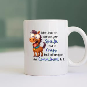 Puede incluir: Taza de cerámica blanca con una ilustración de un caballo de dibujos animados y el texto: "I don't think I've ever seen your Specific Kind of Crazy but I admire your total Commitment to it." La taza tiene un asa curvada.