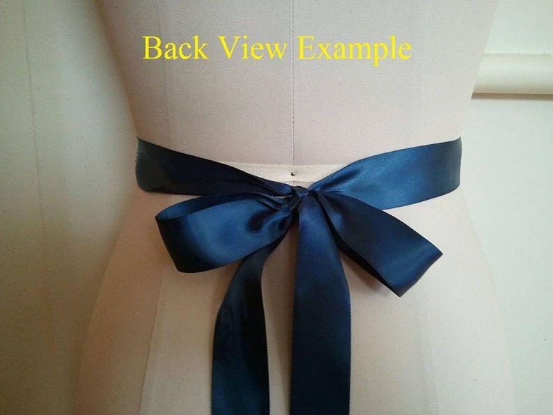 May include: Back view example of a navy blue satin ribbon tied in a bow around a waist.