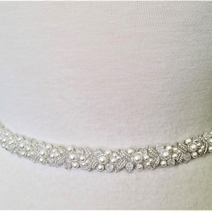 May include: A white beaded bridal sash with pearl and crystal embellishments. The sash is designed to be worn around the waist.