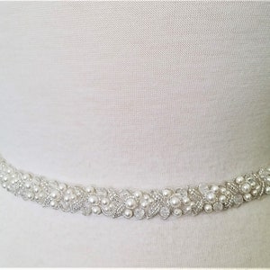 May include: A white beaded bridal belt with pearl and crystal embellishments. The belt is designed to be worn around the waist.