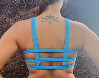 May include: A bright blue sports bra with a racerback design and a criss-cross strap detail in the back. The bra has a geometric dragonfly tattoo on the back.
