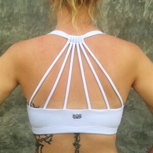 Pu&ograve; includere: Reggiseno sportivo bianco con schiena incrociata e logo a forma di fiore di loto.