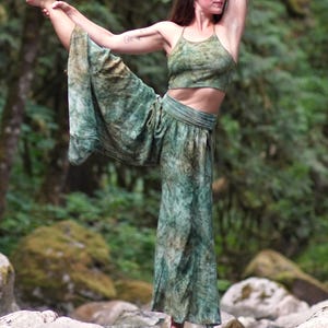 May include: A two-piece set consisting of a cropped halter-style top and wide-leg trousers, both featuring a mottled green and brown tie-dye pattern. The top has thin straps, and the trousers have a high, fitted waistband with loose, flowing legs.
