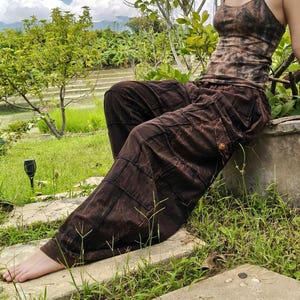 Peut inclure: Un débardeur à fines bretelles marron tie-dye associé à un pantalon cargo marron ample doté de poches latérales et de boutons. Le pantalon présente une construction style patchwork avec des coutures visibles et un motif marron chiné foncé.