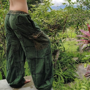 Op de afbeelding: Losvallende olijfgroene broek met een patchworkontwerp met zichtbare donkere stiksels, een elastische tailleband en een grote cargozak aan de zijkant. De broek heeft een wijd uitlopend model en een textuurrijke, doorleefde uitstraling.