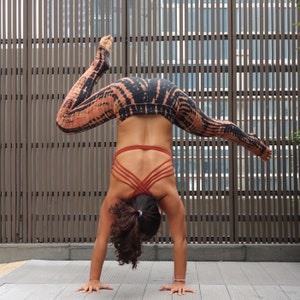 May include: A person doing a handstand in black and orange tie-dye leggings and a red sports bra with criss-cross straps.