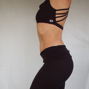 Pode incluir: Capri de yoga preto com cintura larga e um logotipo de flor de lótus na perna esquerda.