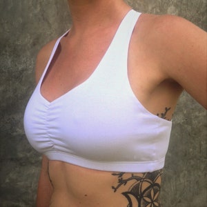 Pu&ograve; includere: Reggiseno sportivo bianco con scollo rotondo e stile racerback. Il reggiseno ha un dettaglio arricciato nella parte anteriore.