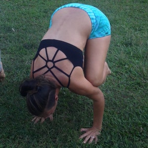 Könnte beinhalten: Eine Frau in einem schwarzen Sport-BH mit geometrischem Muster und blau-weiß gemusterten Shorts macht einen Handstand auf einer grasbewachsenen Fläche.