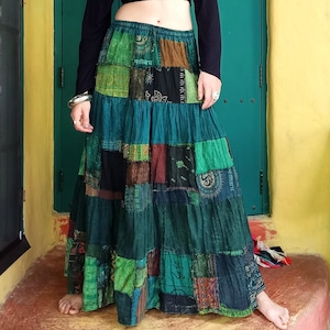 Può includere: Una lunga gonna a strati in patchwork in tonalità di verde, marrone e nero. La gonna è realizzata con diversi tessuti e presenta uno stile unico e bohémien.