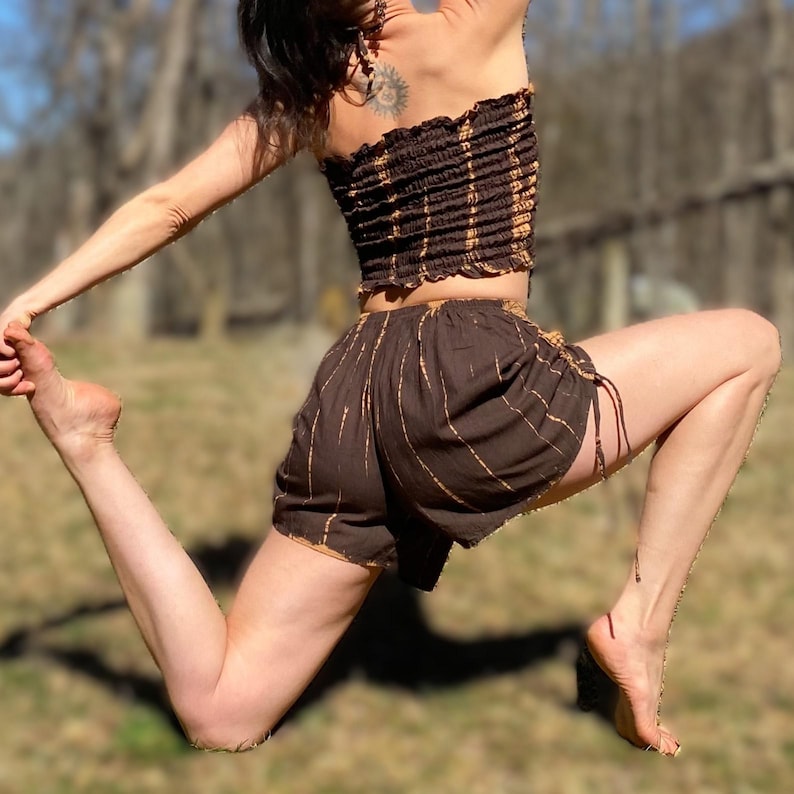 May include: Brown and tan tie-dye two-piece outfit. The top is a strapless tube top with horizontal stripes. The shorts are high-waisted with vertical stripes and drawstring ties. The outfit is made of a soft, flowing fabric.