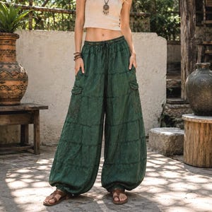 May include: Loose-fitting, dark green wide-leg trousers featuring a drawstring elastic waistband, side cargo pockets, and a horizontal paneled design. The pants have a relaxed, voluminous silhouette that extends to the ankles, paired with brown sandals.