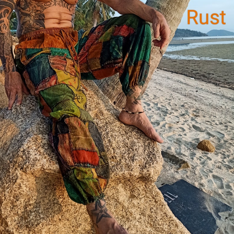 May include: Patchwork pants in shades of green, orange, and brown. The pants have an elastic waistband and cuffs. The image shows the pants on a person sitting on a rock near a beach. The word "Rust" is in the top right corner.