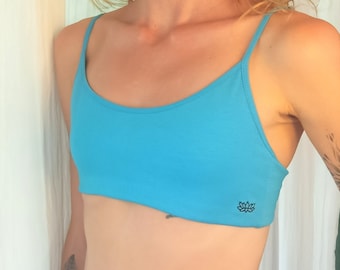 May include: A bright blue cropped tank top with thin straps. The tank top has a small lotus flower logo on the bottom right side.