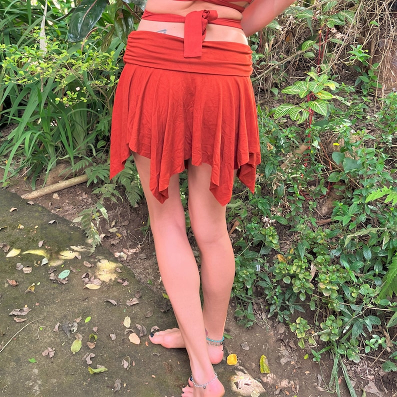 May include: A rust-colored, asymmetrical skirt with a wide waistband. The skirt is made of a soft, flowing fabric and has a relaxed fit.