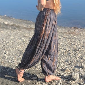 May include: Loose-fitting charcoal gray trousers featuring a gathered elastic waistband and a vertical brown tie-dye stripe pattern running down the sides. The pants have a relaxed, billowy silhouette with tapered, elasticized cuffs at the ankles.