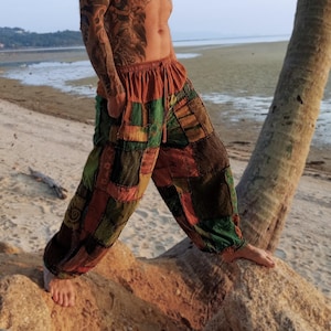 May include: Loose-fitting trousers featuring a patchwork design with various rectangular fabric panels in shades of rust orange, olive green, and dark brown. The pants have an elasticized waistband with a drawstring and a relaxed, wide-leg silhouette.