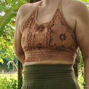 May include: A light brown halter top with detailed embroidery and a fringed hem. The top has floral and geometric patterns. The lower part of the image shows a green skirt. The top is made of a soft, lightweight fabric.