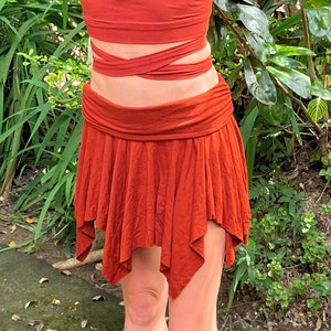 May include: A rust-colored skirt with a gathered waist and a flowing, asymmetrical hemline. The skirt is made of a soft, lightweight fabric and has a relaxed, bohemian style.