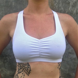 Pu&ograve; includere: Reggiseno sportivo bianco con schienale a sgancio rapido e un dettaglio arricciato sul davanti.