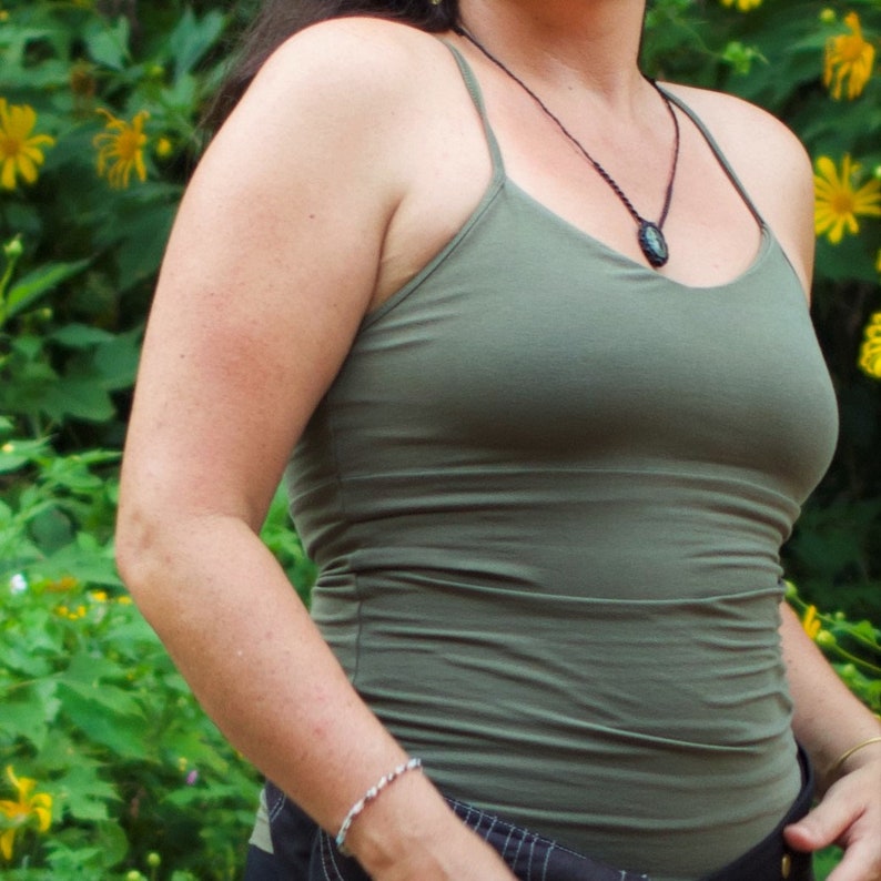 May include: A woman wearing a green tank top with a black pendant necklace. The tank top is a simple, fitted style with a scoop neck.