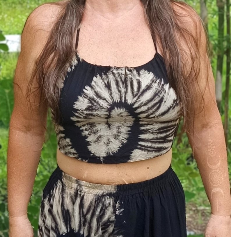 May include: A black and white tie-dye halter top and matching skirt. The top features a circular pattern, and the skirt has a similar design. The outfit is made of a soft, flowing fabric, perfect for warm weather.