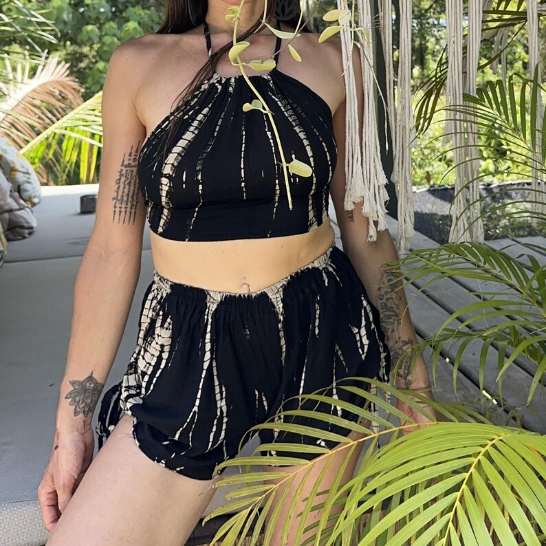 May include: A two-piece matching set featuring a halter top and shorts. The set is black with a white tie-dye pattern. The top has a halter neck and the shorts have an elastic waistband. The outfit is made of a lightweight fabric.