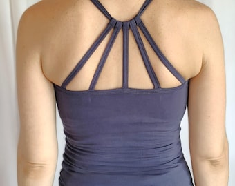 May include: A dark blue vest top featuring a distinctive strappy back. The straps form a geometric design across the upper back. The top is made of a soft, form-fitting material, and the style is casual and sporty.