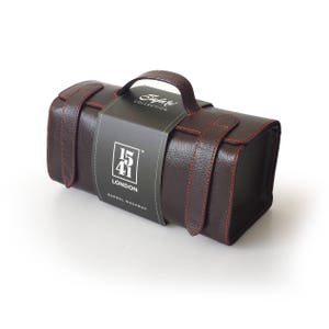 May include: A brown leather barrel washbag with red stitching and a handle. The bag has a black label with the text "1541 LONDON" and "Barrel Washbag". The bag is designed to hold toiletries and other personal items.