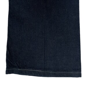 May include: Close-up of the bottom hem of a pair of dark blue denim jeans. The hem is sewn with a straight stitch.