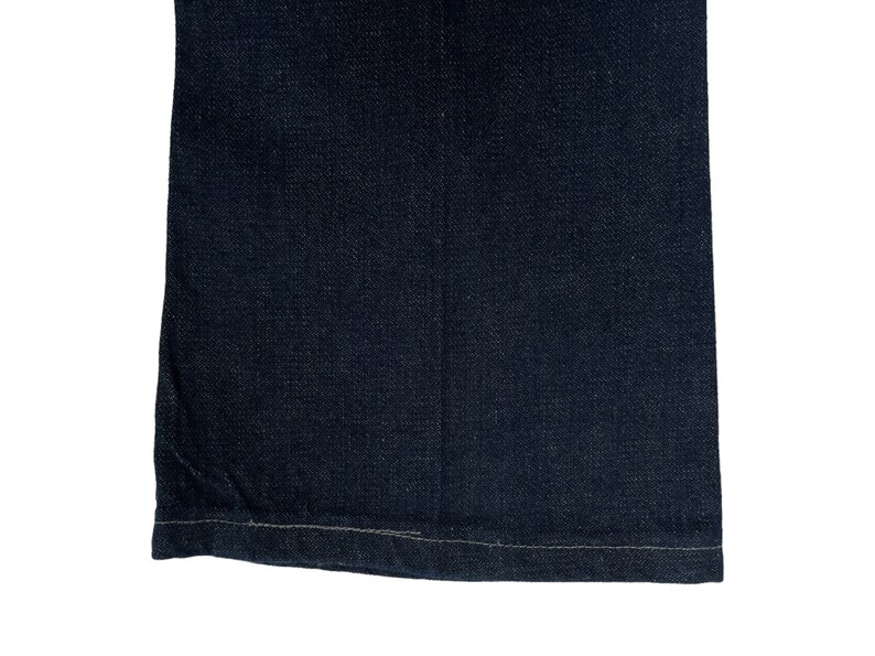 May include: Close-up of the bottom hem of a pair of dark blue denim jeans. The hem is sewn with a straight stitch.