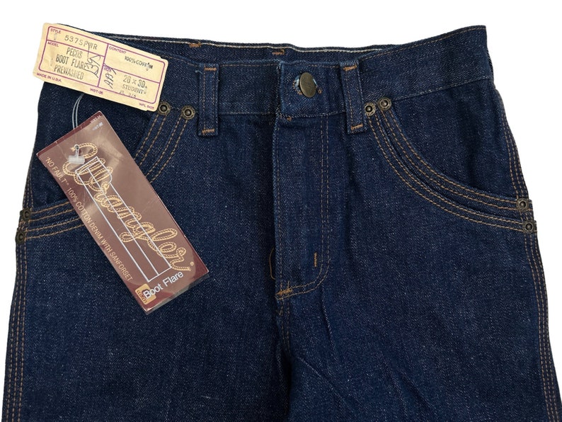 May include: A pair of dark blue denim jeans with a boot flare style. The jeans have a label that reads "Wrangler Boot Flare" and "No Fault 100% Cotton Denim with Sanforset".