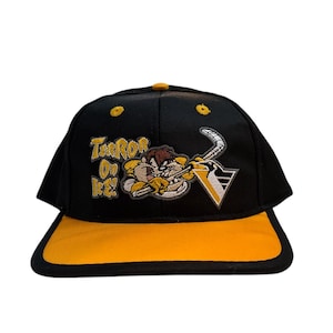 Könnte beinhalten: Schwarze und gelbe Baseballkappe mit einem Cartoon-Tasmanischen Teufel, der ein Hockeytrikot trägt und einen Hockeyschläger hält. Der Text "Terror on Ice" ist auf der Vorderseite der Kappe gestickt.