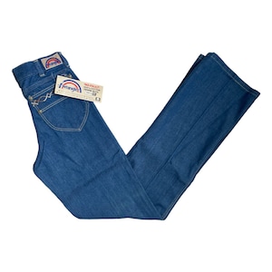 Może przedstawiać: Dżinsy z niebieskiego denimu z metką Wrangler na tylnej kieszeni. Dżinsy mają szerokie nogawki i wysoki stan. Metka na dżinsach głosi "No-Fault 100% Cotton Denim with "W" Stitch".