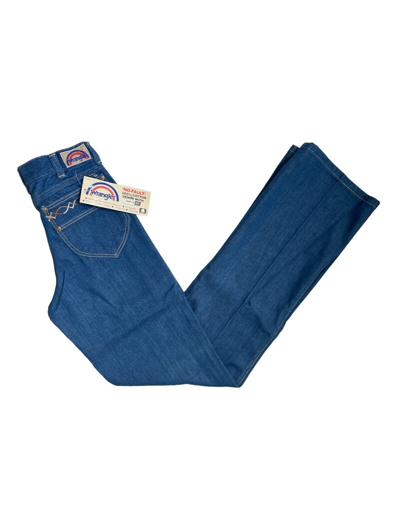 Może przedstawiać: Dżinsy z niebieskiego denimu z metką Wrangler na tylnej kieszeni. Dżinsy mają szerokie nogawki i wysoki stan. Metka na dżinsach głosi "No-Fault 100% Cotton Denim with "W" Stitch".