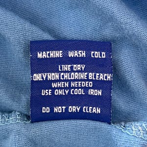 May include: A blue care label with white text that reads "MACHINE WASH COLD, LINE DRY, ONLY NON CHLORINE BLEACH WHEN NEEDED, USE ONLY COOL IRON, DO NOT DRY CLEAN."