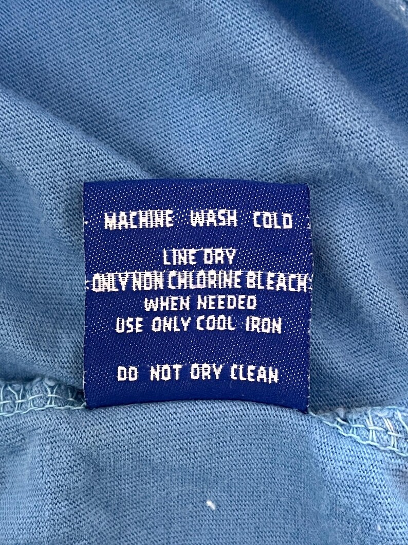 May include: A blue care label with white text that reads "MACHINE WASH COLD, LINE DRY, ONLY NON CHLORINE BLEACH WHEN NEEDED, USE ONLY COOL IRON, DO NOT DRY CLEAN."