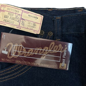 May include: A pair of blue denim jeans with a Wrangler label. The jeans are a boot cut style and have a pre-washed finish. The label says "No Fault" 100% cotton denim with Sanforset. The size tag says 26 x 30, Student.