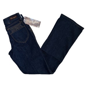 May include: A pair of dark blue denim jeans with a bootcut leg. The jeans have a brown leather patch with the word "Wrangler" on the back waistband.