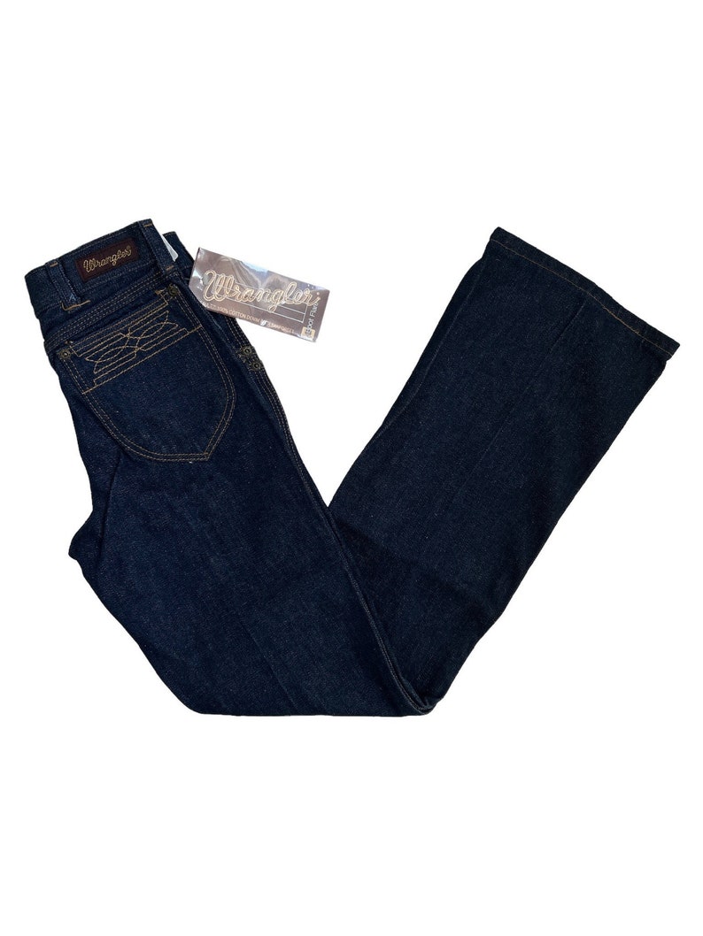 May include: A pair of dark blue denim jeans with a bootcut leg. The jeans have a brown leather patch with the word "Wrangler" on the back waistband.