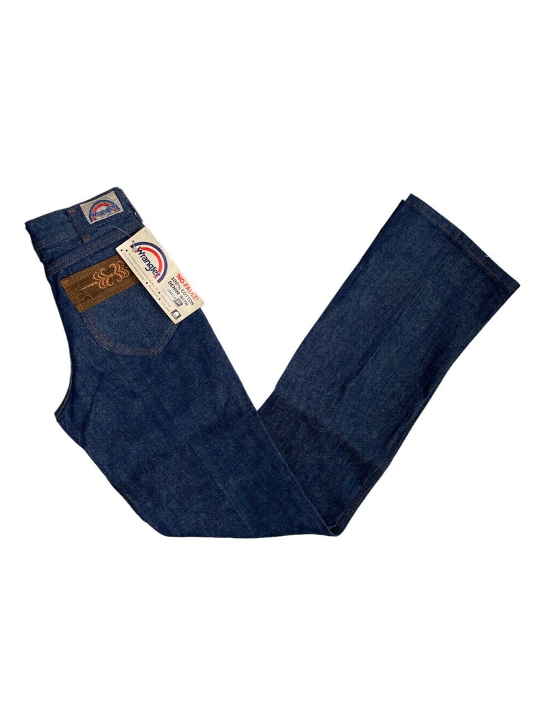 May include: A pair of blue denim jeans with a brown leather patch on the back pocket. The jeans have a Wrangler label and a tag that says "No-Plus Size 100% Cotton Denim Made in USA".