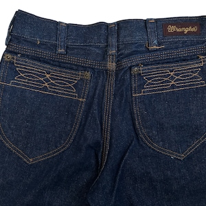 May include: A pair of dark blue denim jeans with a Wrangler label on the back waistband. The back pockets have a unique embroidered design.