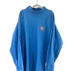 May include: A light blue long-sleeved t-shirt with a small embroidered logo on the front. The logo is a circle with a star inside and the words "Original Vintage" around it.