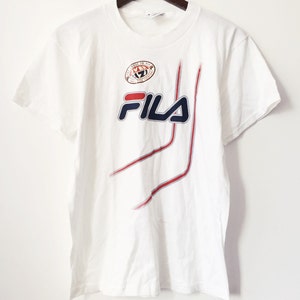 May include: White t-shirt with a blue and red Fila logo and a red, white, and blue circle with the text "The Only Way To Fly" and "Soul Fila Company".