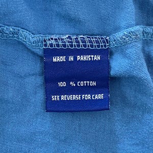 May include: Blue care label with white text that reads "Made in Pakistan", "100% Cotton", and "See Reverse for Care".