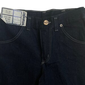May include: A pair of dark blue denim jeans with a silver stud out flare, a Wrangler label, and a size tag that reads "26 x 30 Student".
