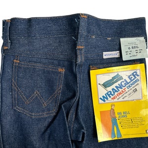 May include: A pair of blue denim jeans with a back pocket featuring the Wrangler logo. The jeans have a label that reads "Wrangler No-Fault Denims 100% Cotton 14 oz. Denims with Sanforized Fit" and "Big Bell Jeans".