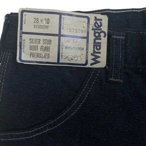 May include: A dark blue denim jean with a silver stud detail. The label reads "26 x 30 Student Silver Stud Boot Flare Prewasjed" and "Wrangler".