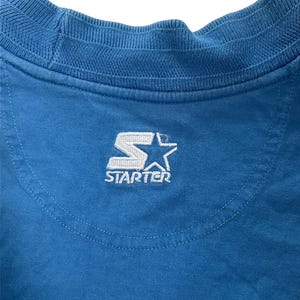 May include: A blue t-shirt with a white embroidered "Starter" logo on the back.