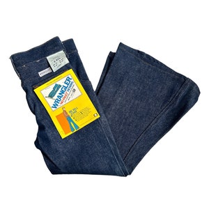 May include: A pair of dark blue denim bell bottom jeans with a yellow and orange Wrangler Big Bell Jeans tag attached. The tag features a cartoon illustration of a person wearing the jeans.